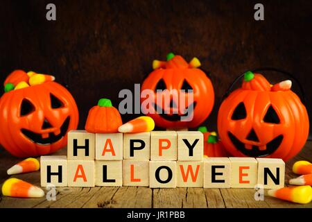 Happy Halloween di blocchi di legno con la caramella di mais e jack o lantern supporti su un arancione e sfondo nero Foto Stock