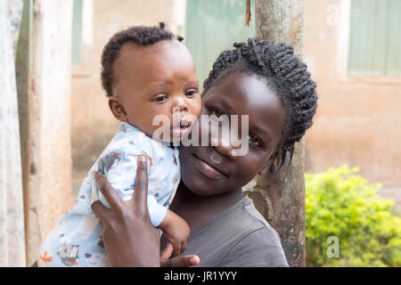 Lugazi, Uganda. 09 giugno 2017. Una giovane ragazza africana mentre tiene il suo fratello bambino nelle braccia Foto Stock