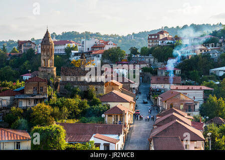 Torre di una chiesa sopra i tetti e i pedoni a piedi giù per una strada di sera; Sighnaghi, Kakheti, Georgia Foto Stock