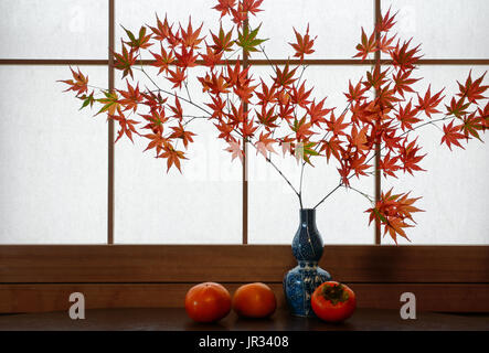 Autunno rustico scena di rosso giapponese foglie di acero e mature, cachi davanti a una carta di riso Sfondo finestra Foto Stock