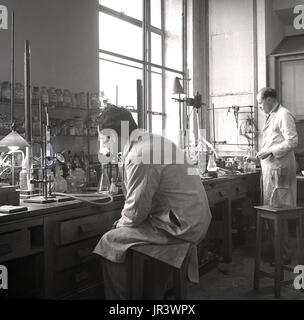 Degli anni Cinquanta, storico, maschio gli scienziati in un laboratorio di conduzione di esperimenti, in corrispondenza di un banco di lavoro in legno, Inghilterra, Regno Unito. Foto Stock