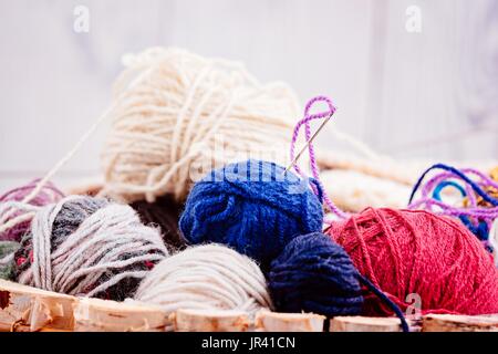 Colorata lana palle e aghi in cesto di legno. Lana per maglieria Foto Stock