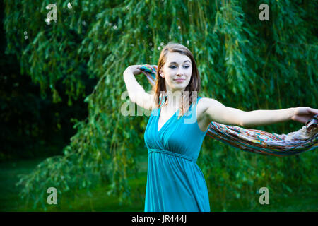 Bella ragazza è lentamente filatura in giro davanti a un salice. Spensierate, felice e gioiosa in un parco durante l'estate. Foto Stock