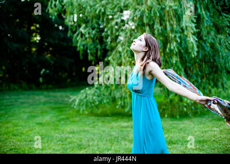 Bella ragazza è lentamente filatura in giro davanti a un salice. Spensierate, felice e gioiosa in un parco durante l'estate. Foto Stock