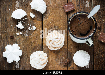 Meringa bianca al buio su un sfondo di legno con metallo retrò tazza da caffè Foto Stock