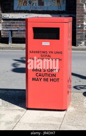 Red spazzatura sul lungomare per BBO solo con testo bilingue indicazione "Attenzione può essere caldo". Aberystwyth, Ceredigion, Wales, Regno Unito, Gran Bretagna Foto Stock