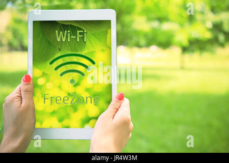 Free zone wi-fi concetto. Tablet con connessione wifi gratuita icona nella donna le mani sul verde sfondo naturale. Accesso gratuito ad internet wi-fi gratuito all'aperto. Foto Stock