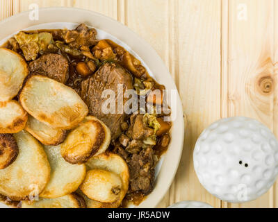 Agnello hotpot con fette di patate e cipolla con sugo di carne contro una luce di legno di pino sullo sfondo di legno Foto Stock