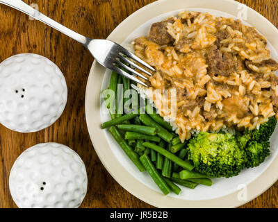 Carni bovine stroganoff con riso a grani lunghi fagiolini e broccoli contro una quercia darl Sfondo legno Foto Stock