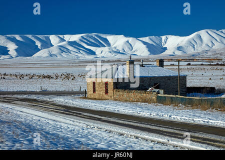 Storico cottage in pietra e gamma di Ida in inverno, Colline Creek, Maniototo di Central Otago, Isola del Sud, Nuova Zelanda Foto Stock