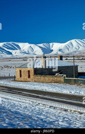 Storico cottage in pietra e gamma di Ida in inverno, Colline Creek, Maniototo di Central Otago, Isola del Sud, Nuova Zelanda Foto Stock