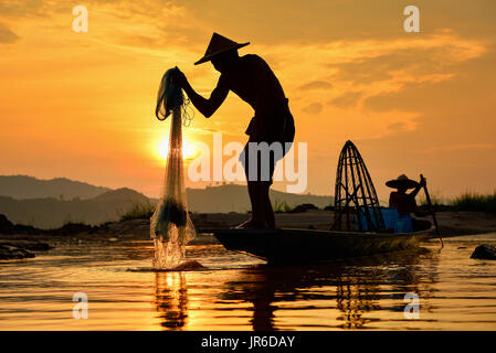 Silhouette di pescatori pesca sollevamento net fuori del fiume al tramonto, Thailandia Foto Stock