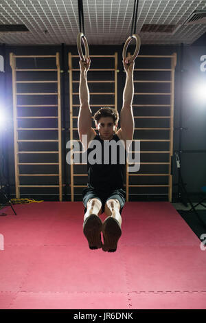 Fitness uomo bello fare immersione esercizio utilizzando anelli in palestra Foto Stock