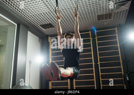 Fitness uomo bello fare immersione esercizio utilizzando anelli in palestra Foto Stock