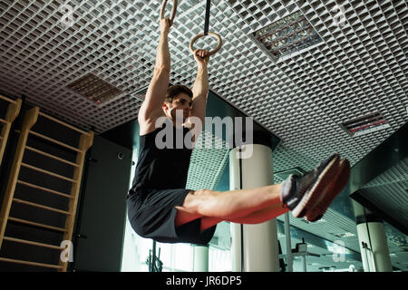 Fitness uomo bello fare immersione esercizio utilizzando anelli in palestra Foto Stock