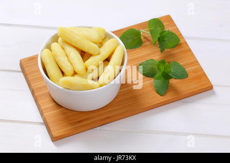 Ciotola di patate cotte coni o gnocchi su tagliere di legno Foto Stock