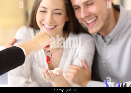 Close up di un felice per i proprietari di ricevere i loro nuove chiavi di casa da un agente immobiliare in ufficio Foto Stock