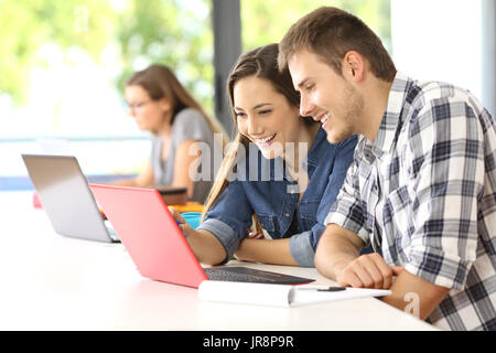 Due studenti di felice apprendimento in linea insieme con un computer in una classe con altri classmate in background Foto Stock