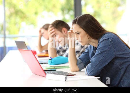 Tre studenti preoccupati cercando di fare un lavoro difficile sulla linea seduto in una scrivania in una classe Foto Stock