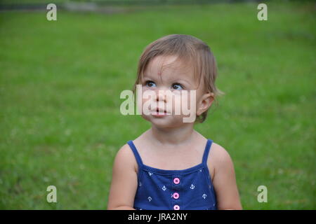 Toddler femmina in piedi fuori con aspetto piacevole sul suo viso. La foto è dalla vita in su. Foto Stock