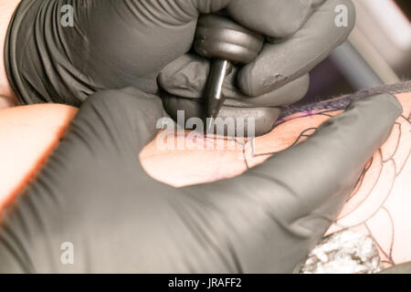 Close up di un tatuaggio artista collocando un tatuaggio usando il suo tatuaggio attrezzature Foto Stock