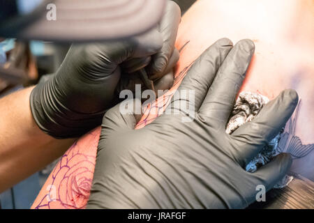 Close up di un tatuaggio artista collocando un tatuaggio usando il suo tatuaggio attrezzature Foto Stock