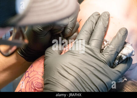 Close up di un tatuaggio artista collocando un tatuaggio usando il suo tatuaggio attrezzature Foto Stock