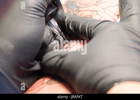 Close up di un tatuaggio artista collocando un tatuaggio usando il suo tatuaggio attrezzature Foto Stock