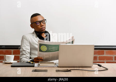 Giovane uomo di affari giornale di lettura alla sua scrivania Foto Stock
