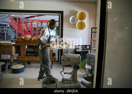 Il panettiere africani che trasportano il vassoio per le pagnotte di pane nel forno Foto Stock