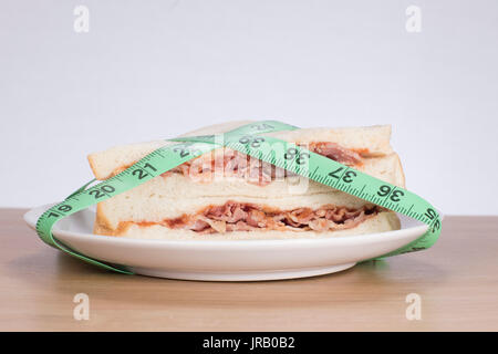 La perdita di peso e la dieta salutare concetto con un gustoso sandwich di pancetta su una piastra avvolto in un nastro verde misurare Foto Stock