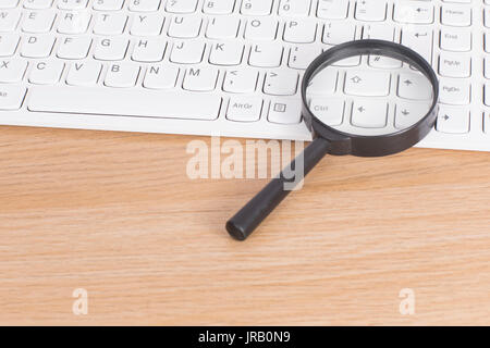 Piccola lente di ingrandimento su un bianco della tastiera del computer giacente su una scrivania di legno in una analisi del business e il concetto di ricerca Foto Stock