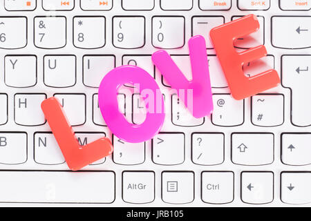 La parola amore di colorati di rosso e rosa lettere giocattolo su bianco della tastiera del computer in pieno il telaio dal concetto di cui sopra Foto Stock
