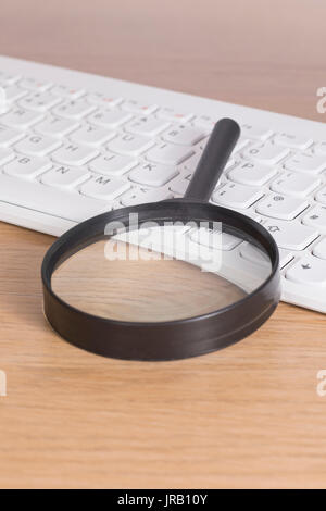 Lente di ingrandimento di plastica nera che stabilisce su bianco tastiera PC sulla scrivania in legno, close-up da un angolo alto Foto Stock