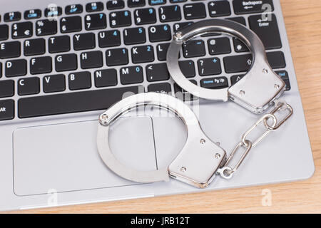 Manette manacles o su un computer portatile che giace sulla tastiera concettuale del internet o di frodi online e la criminalità Foto Stock