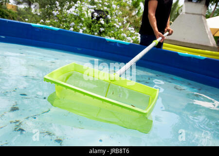 Primo piano di un giovane uomo caucasico pulizia della acqua di un portatile di piscina situata nel cortile con una foglia skimmer montato in un pol telescopico Foto Stock