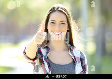 Vista frontale di un felice ragazza gesticolando Thumbs up e guardando a voi soli in strada Foto Stock