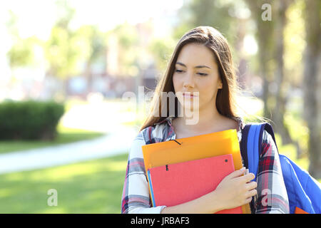 Vista anteriore verticale di un triste studente a piedi in strada tenendo le cartelle all'aperto in un parco Foto Stock