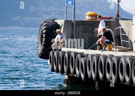 Gli uomini norvegesi con canne da pesca in Norvegia fjord pesca nel campo Porta locale per nave docking Foto Stock