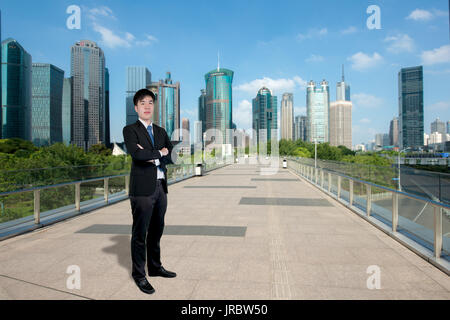 Imprenditore asiatici in piedi con le braccia incrociate con Shanghai lujiazui finance e il quartiere degli affari della zona commerciale grattacielo a Shanghai in Cina Foto Stock