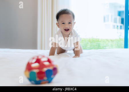 Gattona baby boy sul letto in camera da letto a casa e ha sorriso a voi, bambino asiatico. Foto Stock