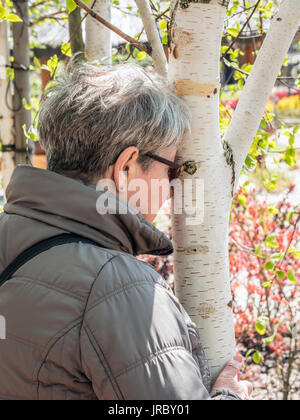 Senior lady abbracciando white birch tronco di albero Foto Stock