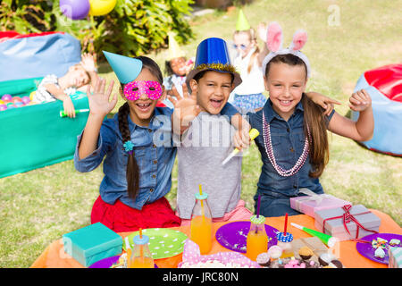 Ritratto di bambini gesticolando mentre è seduto al tavolo in giardino durante il party Foto Stock