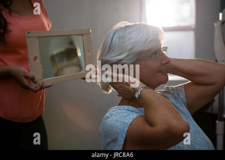 Sezione mediana di un parrucchiere che mostra i capelli in specchio per senior donna al salon Foto Stock