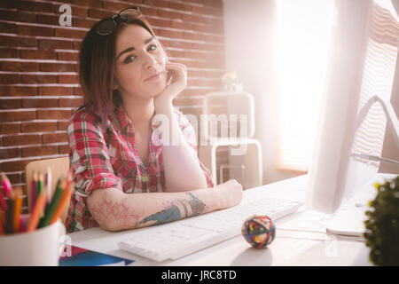 Ritratto di sorridente seduta esecutivo con la mano sulla faccia in ufficio Foto Stock