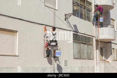 Due pittori in harnasses sbiancamento una parete in Portogallo Foto Stock
