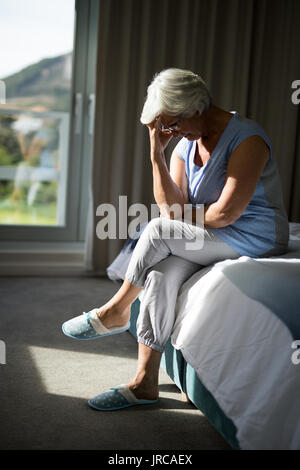 Tense senior donna seduta sul letto in camera da letto a casa Foto Stock