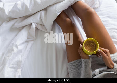 Sezione mediana della donna azienda tazza da caffè mentre vi rilassate sul letto Foto Stock