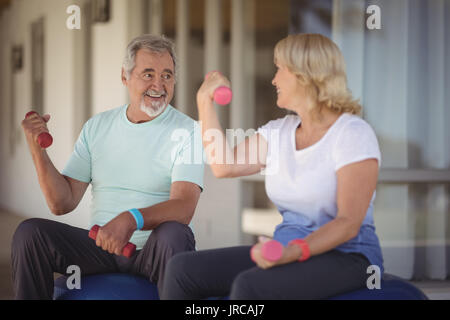 Coppia senior il sollevamento pesi seduti sulla palla ginnica in veranda Foto Stock