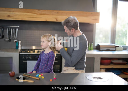 Padre figlie fissante per capelli permanente, mentre in cucina Foto Stock